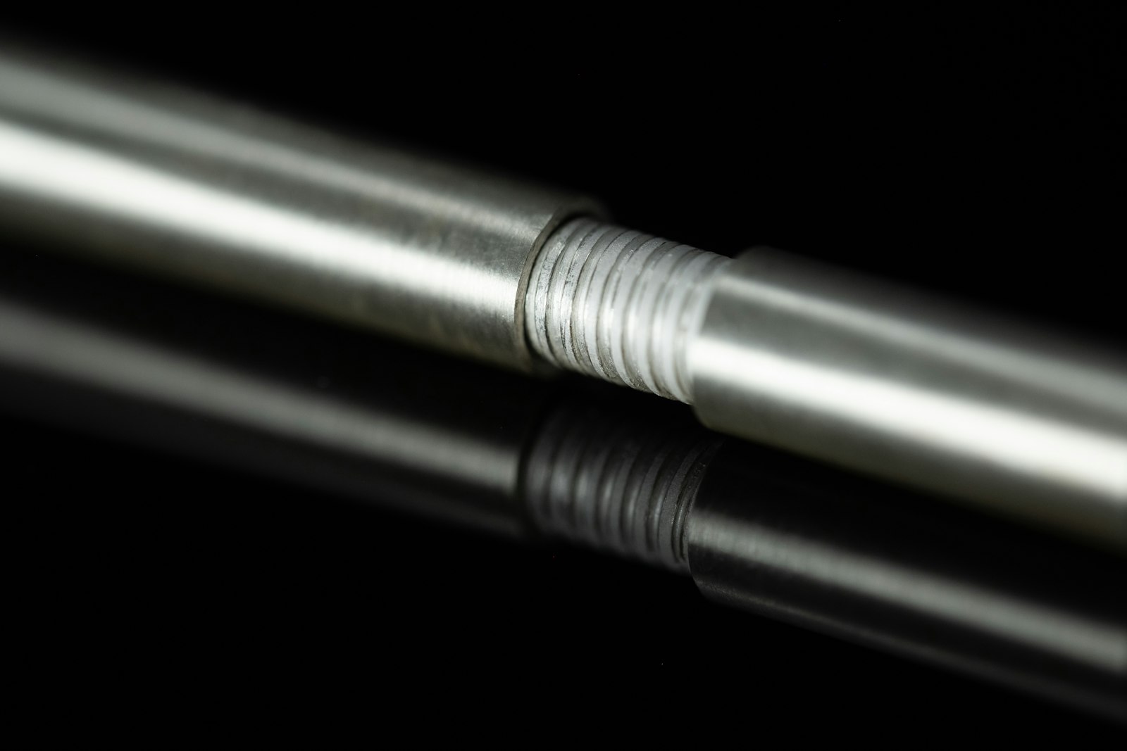 Threaded metal rod with a reflective finish lying on a black surface