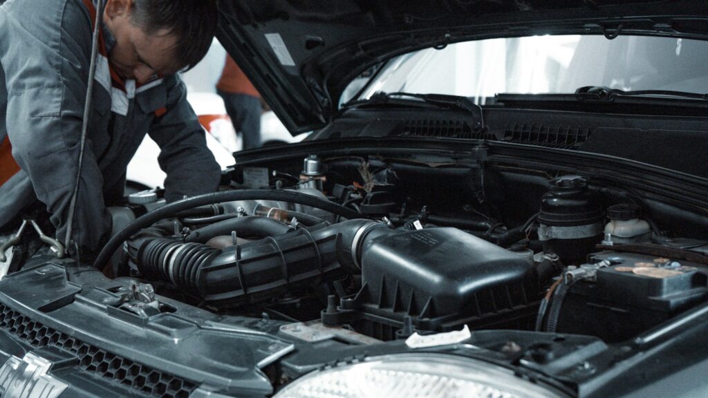 Mechanic in a grey uniform inspecting the engine of a car during a vehicle check