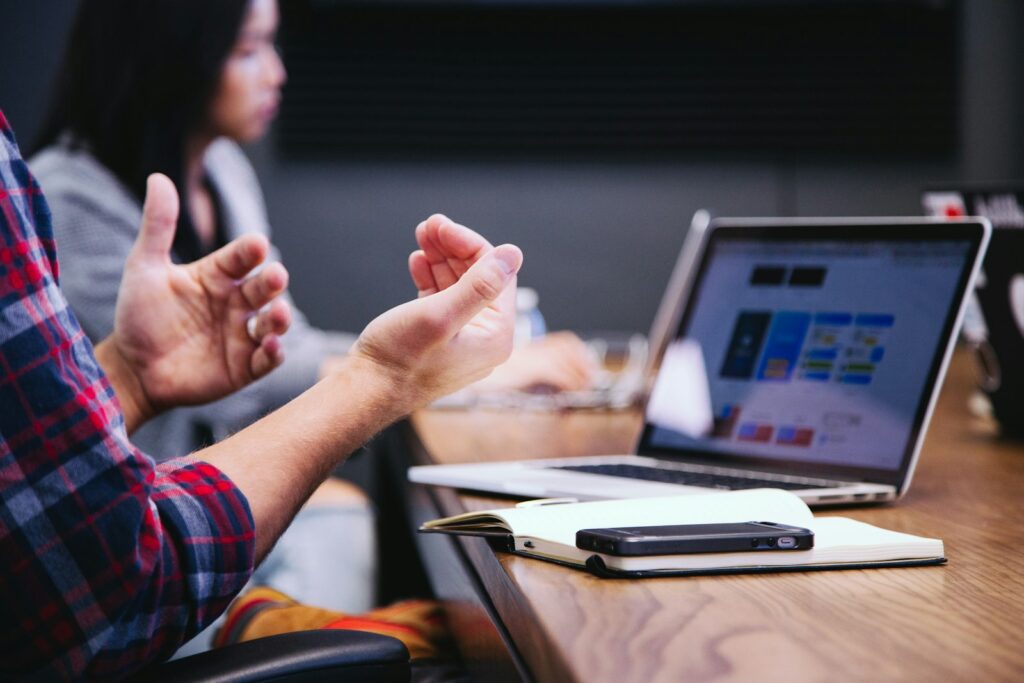 Person gesturing while talking through ideas in a meeting, with a laptop on the table