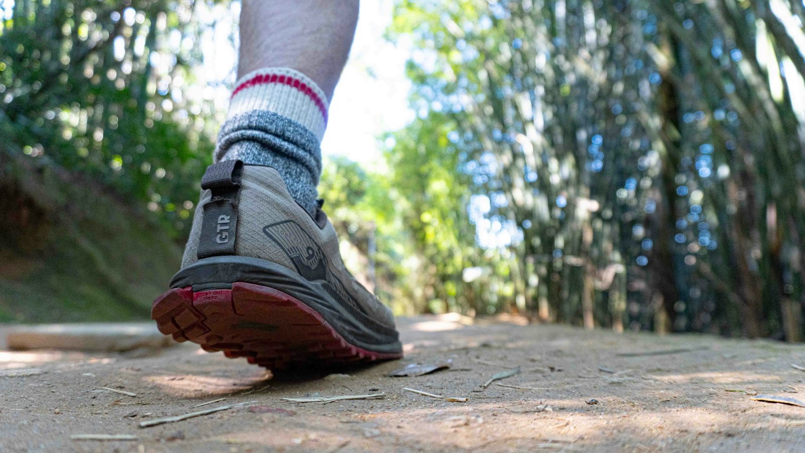 Person wearing a trail running shoe and wool socks standing on a dirt path