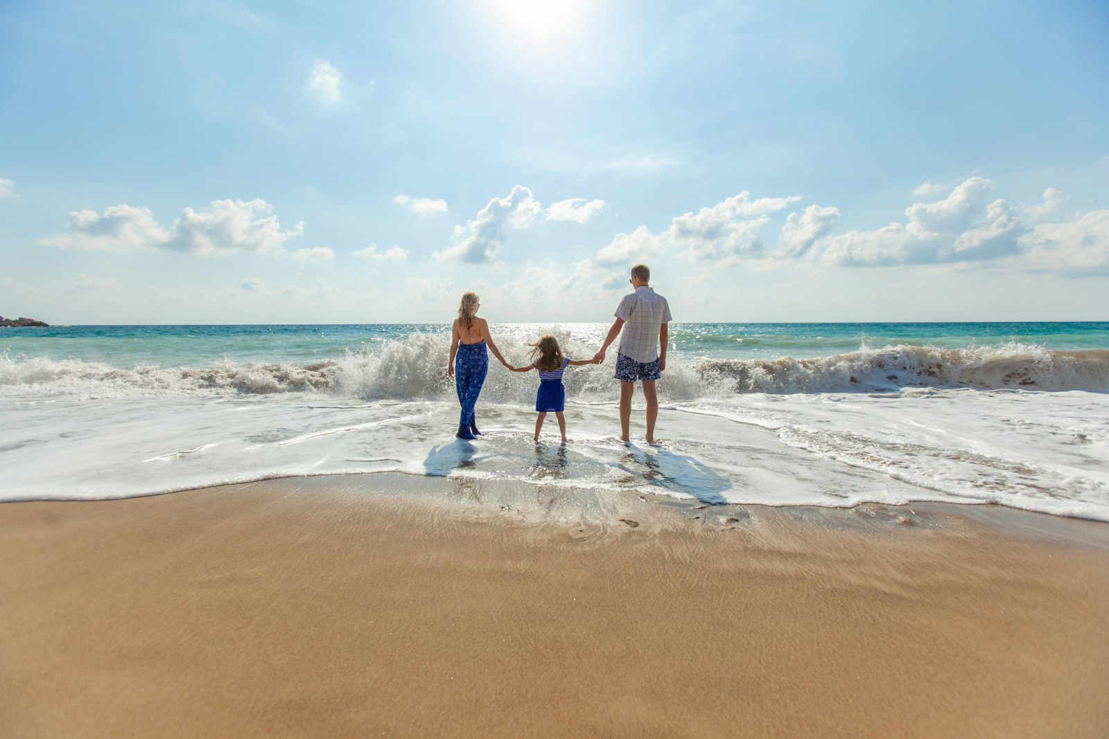 Man, woman and child holding hands as they walk along the seashore
