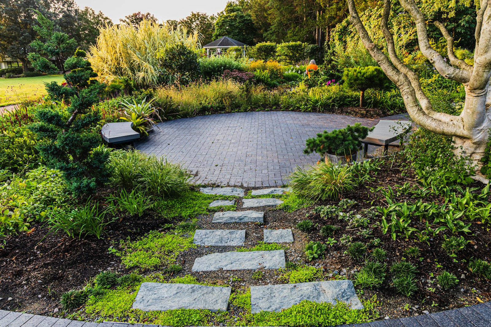 Stone path leading to a circular paved patio surrounded by lush green garden planting